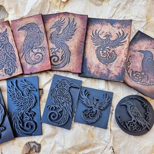 Könnte beinhalten: Ein Set mit neun Holzstöcken, die verschiedene Fabelwesen zeigen, darunter Eulen, Raben und Phönixe. Die Stempel sind mit komplizierten Designs geschnitzt und bereit für Bastel- und Kunstprojekte.