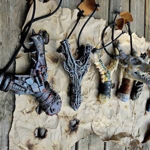 Può includere: Un assortimento di fionde artigianali con design unici ispirati alla fantasia. Le fionde presentano dettagli intricati, tra cui elementi in metallo, legno e osso, con una varietà di colori e trame. Ogni fionda è sospesa da un cavo nero su uno sfondo di legno rustico.