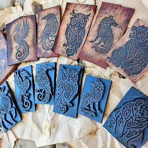 May include: A set of 10 woodblock stamps featuring Celtic knotwork designs of various animals, including a deer, a phoenix, a raven, an owl, a wolf, and a bear. The stamps are made of dark wood and have a black finish.