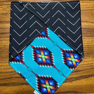 May include: A square pet bandana with a black and white chevron pattern on one side and a turquoise geometric design on the other. The geometric pattern features colorful diamond shapes with red, blue, yellow, and green accents.
