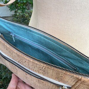 Puede incluir: Un bolso de mano de corcho con cierre de cremallera y forro de tela turquesa. El bolso tiene un asa superior y un bolsillo con cremallera en la parte delantera.