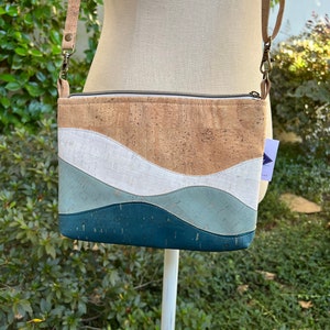 Puede incluir: Un peque&ntilde;o bolso bandolera de corcho y cuero con cierre de cremallera. El bolso tiene un dise&ntilde;o ondulado en tonos azules, blancos y marrones.