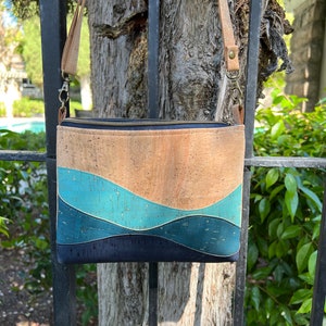 Puede incluir: Un bolso bandolera de corcho y tela con un patr&oacute;n ondulado azul y marr&oacute;n. El bolso tiene una cremallera y una correa larga ajustable.