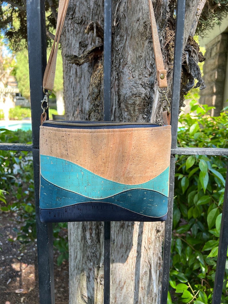 Puede incluir: Un bolso bandolera de corcho y tela con un patr&oacute;n ondulado azul y marr&oacute;n. El bolso tiene una cremallera y una correa larga ajustable.