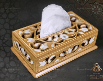 May include: A wooden tissue box cover with intricate floral carvings and mother-of-pearl inlay. The box is light brown with white accents and has a rectangular shape.