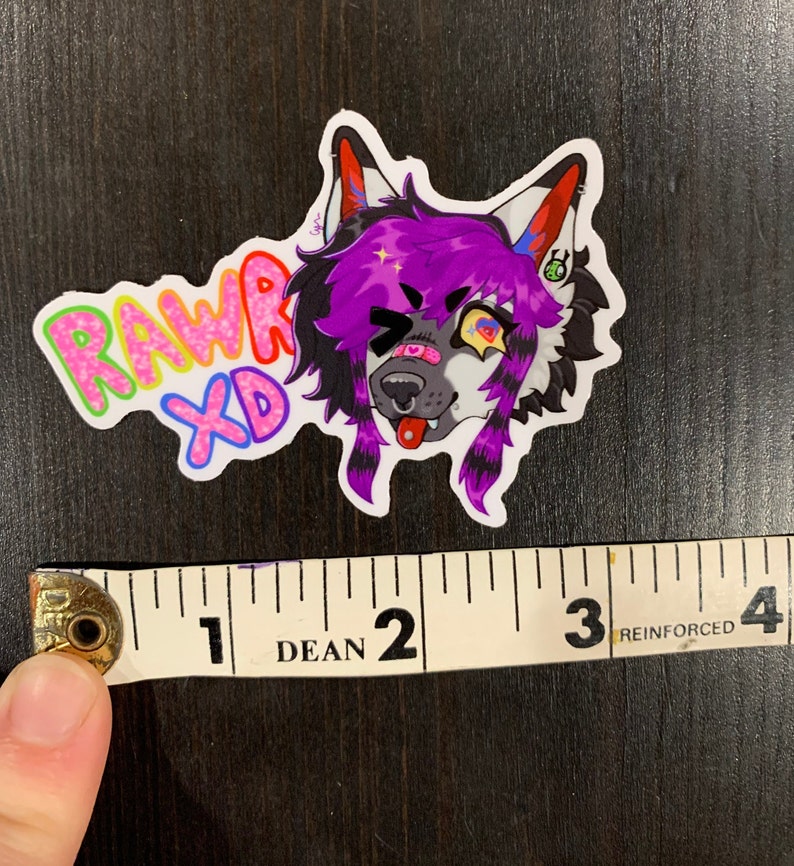 May include: A colorful sticker featuring a cartoon wolf with purple hair, a winking eye, and a tongue sticking out. The sticker has the text "RAWR XD" in rainbow colors. The sticker is approximately 3 inches wide.