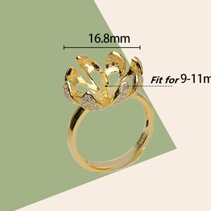 May include: Gold ring with a flower-shaped setting, 16.8 mm in diameter, designed to hold a pearl or gemstone. The setting is decorated with small clear stones.  Fit for 9-11 mm pearls.