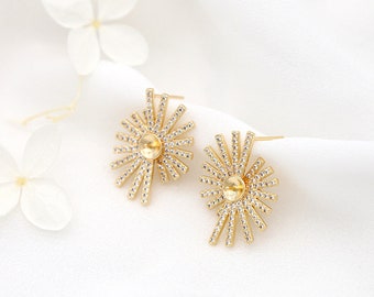 May include: A pair of gold earrings with a sunburst design. The earrings are adorned with small, clear crystals and have a round, clear centre stone.