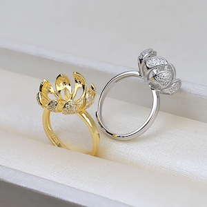 May include: Two rings with a flower design, one is gold and the other is silver. Both rings are adorned with small clear stones.