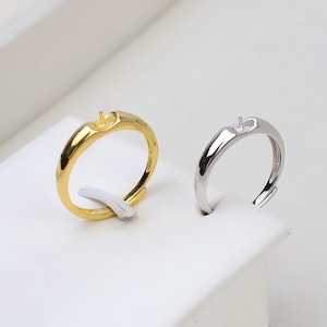 May include: Two adjustable rings with a small hole on top for adding a pearl or other embellishment. The ring on the left is gold and the ring on the right is silver.
