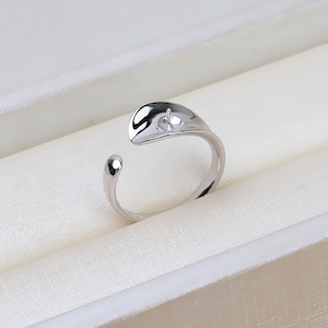 May include: A silver ring with a smooth, curved design. The ring has a small hole in the center, which is designed to hold a pearl or other gemstone.