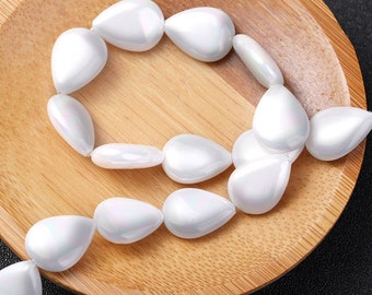 May include: A strand of white teardrop-shaped beads on a wooden surface. The beads have an iridescent finish.