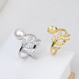 Puede incluir: Dos anillos de plata y oro con un diseño de hoja y piedras transparentes. Un anillo tiene una perla en el extremo de la hoja. Ambos anillos son ajustables.