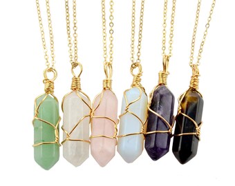 May include: Seven gold necklaces with different colored crystal pendants. The pendants are wrapped in gold wire and have a pointed shape. The crystals are green, white, pink, blue, purple, and brown.