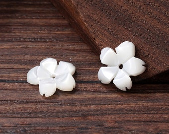 Könnte beinhalten: Zwei weiße Muschelknöpfe in Blumenform mit einem Loch in der Mitte. Die Knöpfe liegen auf einer Holzoberfläche.