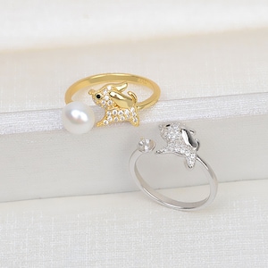 Puede incluir: Dos anillos ajustables con un pequeño diseño de perro detallado. Un anillo es dorado con un acento de perla, y el otro es plateado.