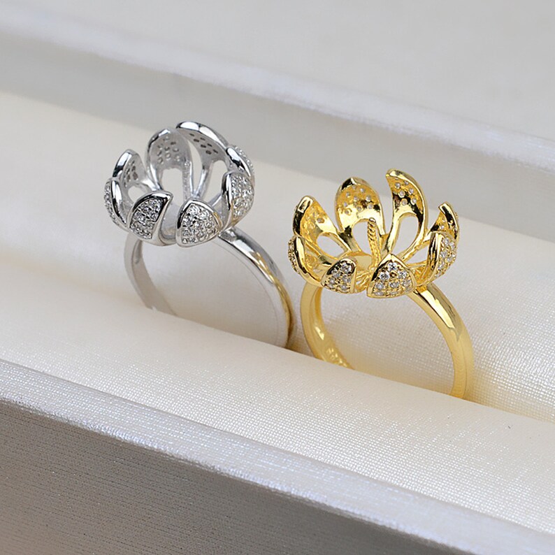 May include: Two ring settings with a flower-shaped design. One is silver with clear stones and the other is gold with clear stones.