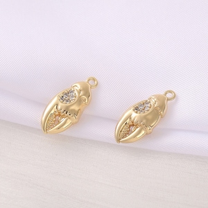 May include: Two gold-toned metal charms shaped like a crab claw with clear crystal accents.