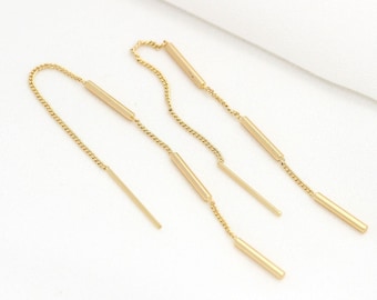 May include: A pair of gold-toned chain earrings with multiple dangling bars. The earrings are made of a thin chain with small, round links. Each earring has three bars that dangle from the chain. The bars are all the same length and width, and they are all made of a smooth, shiny metal.