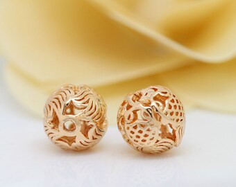 May include: Two gold-colored metal beads with intricate, openwork designs. The beads are round and have a delicate, filigree pattern.