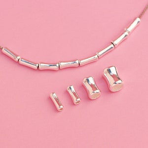 May include: Silver metal beads in various sizes, including a long strand of beads and four individual beads. The beads are all cylindrical in shape and have a smooth, polished finish.