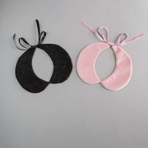 May include: Two detachable collars: one black with a textured pattern and black ribbon ties, and one pink velvet with a pink velvet ribbon tie. The collars are circular with a split design.