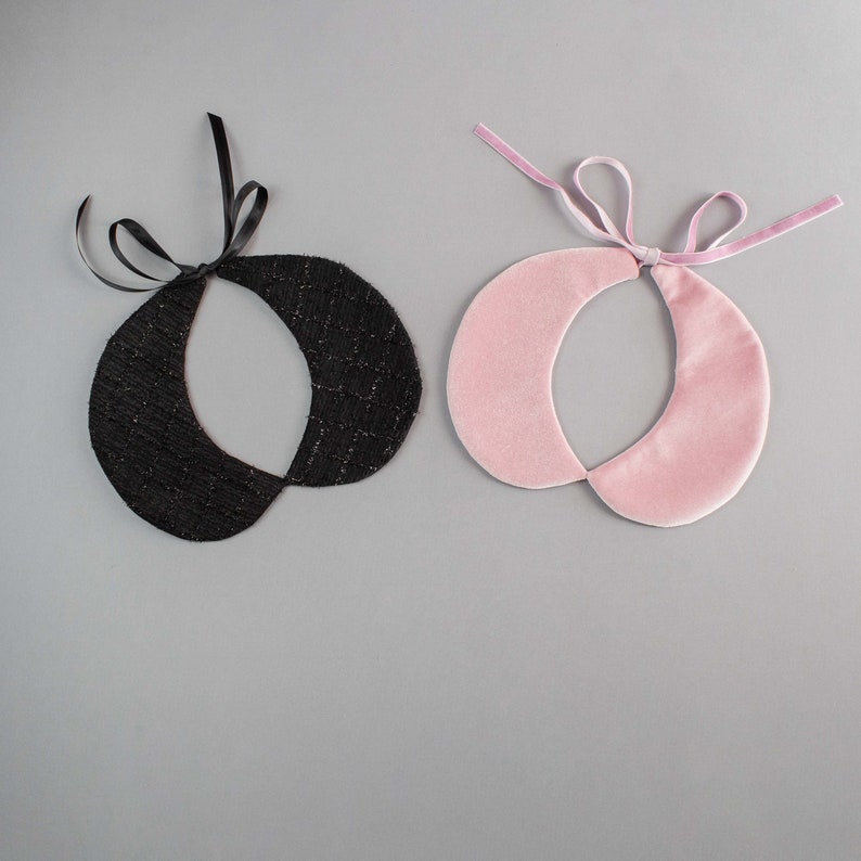 May include: Two detachable collars: one black with a textured pattern and black ribbon ties, and one pink velvet with a pink velvet ribbon tie. The collars are circular with a split design.