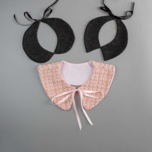May include: Three decorative collars. Two are black with a textured appearance and black ribbon ties. The third collar is pink and white tweed with a pink ribbon bow. The collars are on a gray background.
