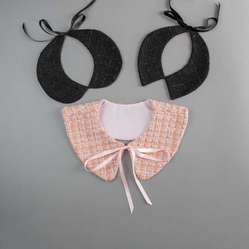 May include: Three decorative collars. Two are black with a textured appearance and black ribbon ties. The third collar is pink and white tweed with a pink ribbon bow. The collars are on a gray background.