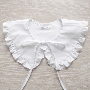 May include: White cotton peter pan collar with a ruffled edge and a bow tie. The collar has a label that says "MokushiAri".