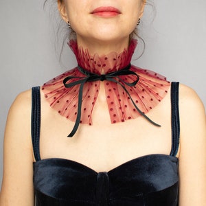 Puede incluir: Un collar de encaje burdeos con lunares negros y un lazo de terciopelo negro. El collar lo lleva una persona con un top de terciopelo negro.