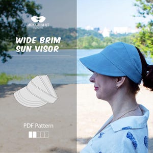 Op de afbeelding: Een lichtblauwe zonneklep met een brede rand en een gestructureerd ontwerp. De afbeelding bevat de tekst MOKUSHART patterns, WIDE BRIM SUN VISOR en PDF Pattern, samen met een lijntekening van de klep en een icoon van vier vierkantjes.