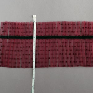 Puede incluir: Primer plano de una tela de tul burdeos con lunares blancos. La tela est&aacute; plisada y mide aproximadamente 15 cm de largo. Una cinta negra est&aacute; cosida en la parte superior de la tela.