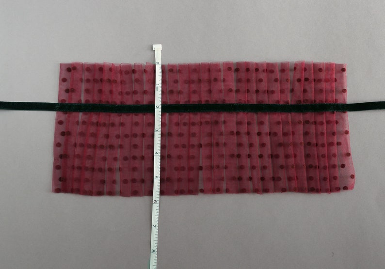 Puede incluir: Primer plano de una tela de tul burdeos con lunares blancos. La tela est&aacute; plisada y mide aproximadamente 15 cm de largo. Una cinta negra est&aacute; cosida en la parte superior de la tela.