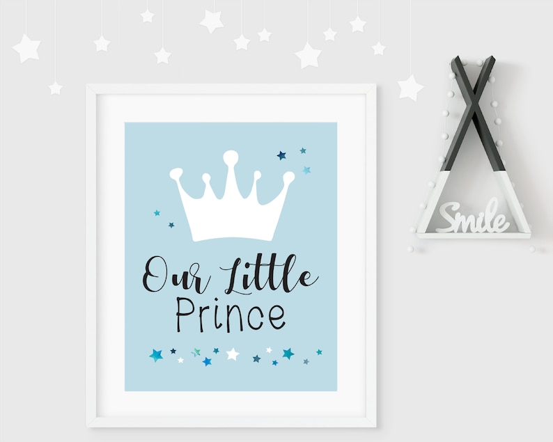 May include: A white framed print with a light blue background. The print features a white crown with a black inscription that reads "Our Little Prince". The background is decorated with small blue and white stars.