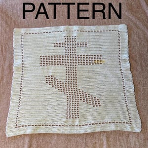 Puede incluir: Cuadrado de ganchillo color crema con un gran diseño de cruz en el centro. La palabra "PATTERN" está impresa en negro en la parte superior. La cruz está hecha con espacios abiertos y los bordes tienen un borde decorativo.