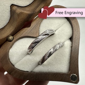 May include: Two silver wedding bands with a textured design, displayed in a wooden heart-shaped box. The box has a velvet lining and the text "Free Engraving" is visible on the box.