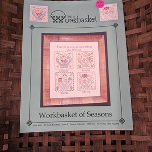 May include: A Workbasket of Seasons cross-stitch pattern. The design features four seasonal images: Summer, Autumn, Winter, and Spring. The text "There is no season such delight can bring as" is above the images. The Workbasket logo is at the top.