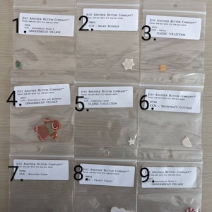 May include: Nine individual plastic bags, each containing a different button design. The bags are labeled with the company name "Just Another Button Company" and a product code. The buttons are themed around Christmas and winter holidays.