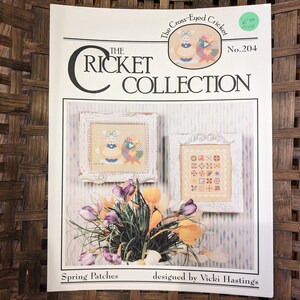 May include: Cross stitch pattern booklet titled "The Cross-Eyed Cricket" with the number 204. The pattern is called "Spring Patches" and is designed by Vicki Hastings. The booklet features two images of cross stitch patterns, one of a pair of birds and the other of a patchwork quilt.