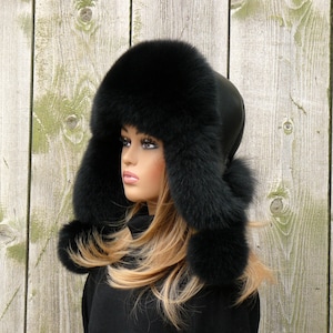May include: A black fur hat with ear flaps. The hat is made of real fur and has a leather band around the crown.
