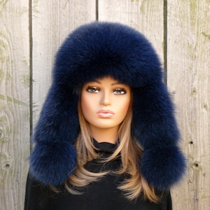 May include: A navy blue faux fur hat with ear flaps. The hat has a pom-pom on each ear flap.