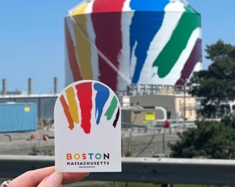 May include: A white die-cut sticker featuring a colorful graphic of vertical brushstrokes in yellow, orange, red, blue, green, and purple. Below the graphic, the text reads BOSTON MASSACHUSETTS in black, with the letter O replaced by a colorful dot.