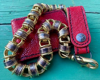 May include: A red leather wallet with a gold chain made of US coins. The chain is made of multiple linked rings, each with a different US coin design. The wallet has a flap with a stitched edge and a silver button.