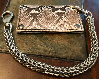 May include: A brown and white snakeskin wallet with a silver chain attached. The chain is made of interwoven metal links.