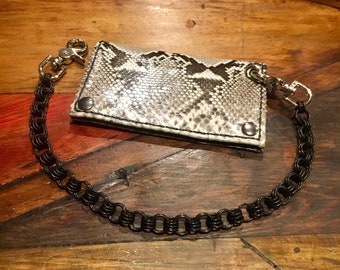 May include: A black chain wallet with a snakeskin pattern. The wallet is attached to a thick black chain.