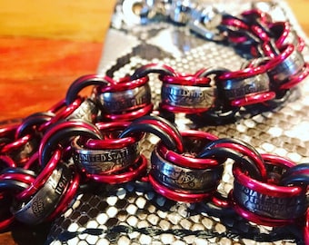 May include: A close-up of a chain made from US quarter coins, with red and black braided cord. The chain is lying on a snakeskin-patterned surface.