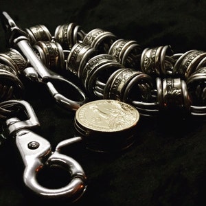 Puede incluir: Una cadena de plata hecha de monedas de dólar estadounidense enlazadas con un cierre y un gancho de plata. La cadena está sobre una superficie negra.