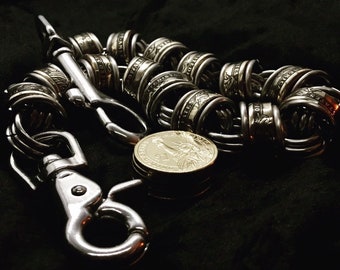 May include: A silver chain made of linked US dollar coins with a silver clasp and a silver hook. The chain is lying on a black surface.