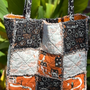 May include: A quilted tote bag featuring a patchwork design of Halloween-themed fabric squares in black, white, and orange. The fabric displays patterns of skulls, ghosts, pumpkins, spiders, and houses, with the text Happy Halloween visible.